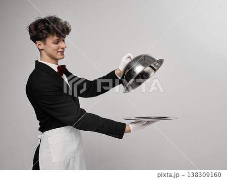 Waiter lifting cloche lid from tray in clean studio environment revealing serving gesture. Waiter lifting cloche lid from tray in clean studio environment revealing serving gesture. 138309160