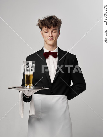 Waiter looking down at beer glass on tray in minimal studio composition. Waiter looking down at beer glass on tray in minimal studio composition. 138309279