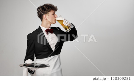 Waiter drinking beer in formal uniform with tray in minimal studio setting Waiter drinking beer in formal uniform with tray in minimal studio setting 138309281