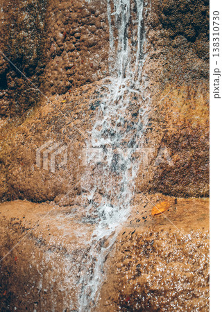 Closeup of water flowing over textured rock surface creating natural abstract pattern and motion, Minimal cascade detail with wet stone and dynamic water splash in tropical environment Closeup of water flowing over textured rock surface creating natural abstract pattern and motion, Minimal cascade detail with wet stone and dynamic water splash in tropical environment 138310730