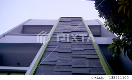 Looking up to a modern apartment building with green tiled roof. 138311106