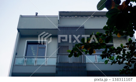 Facade of a modern house building with green leaves in the foreground. comfortable residential home. Facade of a modern house building with green leaves in the foreground. comfortable residential home. 138311107