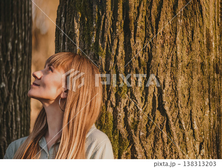 Peaceful Young Woman Leaning Against Tree 138313203