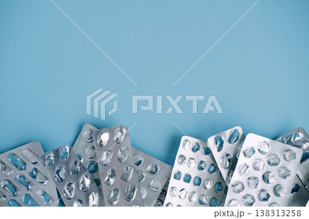 Empty silver blister packs form border at bottom of blue background. Non-recyclable medical waste, plastic pollution in healthcare, eco-friendly pharmacy. Empty silver blister packs form border at bottom of blue background. Non-recyclable medical waste, plastic pollution in healthcare, eco-friendly pharmacy. 138313258