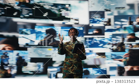 Military commander in war communicating enemy activity to troops, following them using videowall. Military dispatcher wearing headset speaking about enemy threats seen on digital display, camera A 138313523