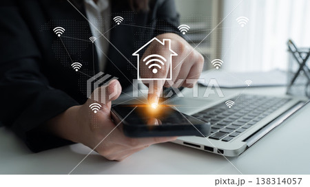 Modern Smart Home Technology Concept with User Interacting on Smartphone, Wi-Fi Signals, and Laptop in Background in Contemporary Office Setting Gantry 138314057