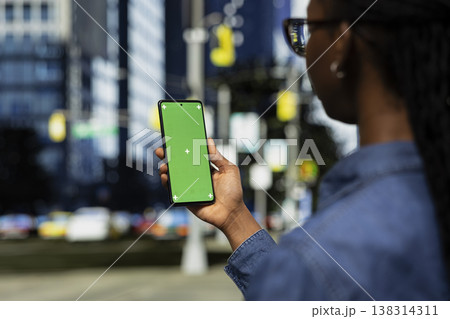 Isolated screen smartphone used by woman walking on city street and looking at social media posts. African american girl on downtown metropolitan area avenue scrolling on mockup mobile phone Isolated screen smartphone used by woman walking on city street and looking at social media posts. African american girl on downtown metropolitan area avenue scrolling on mockup mobile phone 138314311