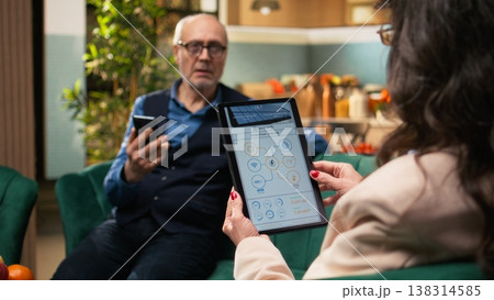 Senior woman holding tablet with green energy systems relaxing at home, healthy lifestyle together with renewable solar power. Zero emission and sustainability shape eco-conscious household. Senior woman holding tablet with green energy systems relaxing at home, healthy lifestyle together with renewable solar power. Zero emission and sustainability shape eco-conscious household. 138314585