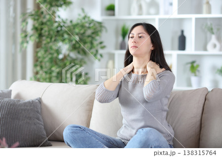 Tense woman massaging her neck at home 138315764