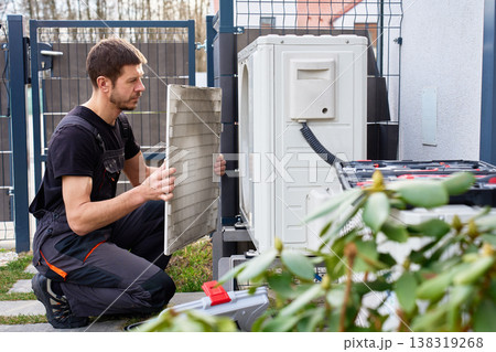 Technician servicing outdoor air source heat pump unit near house wall 138319268