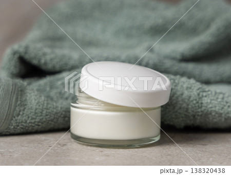 Opened blue cosmetic cream jar with white lid on grey stone near green leaves and bath towel mockup Opened blue cosmetic cream jar with white lid on grey stone near green leaves and bath towel mockup 138320438