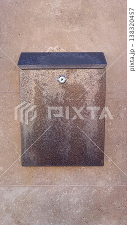 Modern metallic locking mailbox mounted on a textured stone wall of a residential building exterior 138320457