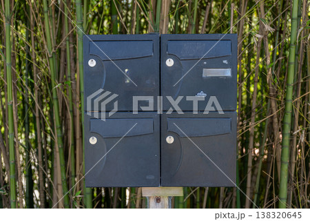Black outdoor mailbox unit with multiple compartments installed on wooden post near bamboo fence residential mail system Black outdoor mailbox unit with multiple compartments installed on wooden post near bamboo fence residential mail system 138320645