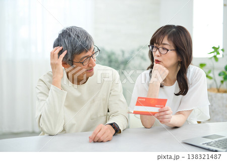 リビングで貯金通帳を見る60代の夫婦 138321487