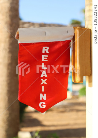 A warning flag under an umbrella on the beach with the inscription We are relaxing, do not disturb A warning flag under an umbrella on the beach with the inscription We are relaxing, do not disturb 138322241