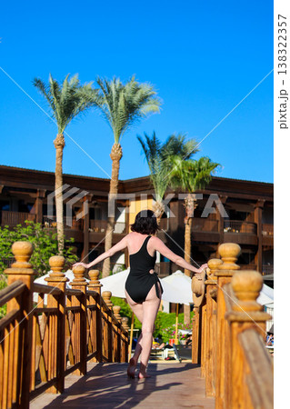 A woman in a bikini stands on a bridge over a hotel swimming pool 138322357