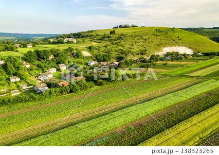 Aerial view of a small village win many houses and green agricultural fields in spring with fresh vegetation after seeding season on a warm sunny day. Aerial view of a small village win many houses and green agricultural fields in spring with fresh vegetation after seeding season on a warm sunny day. 138323265