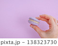 Woman hand holding single lilac macaron close up, demonstrating crispy texture and cream filling of french pastry 138323730