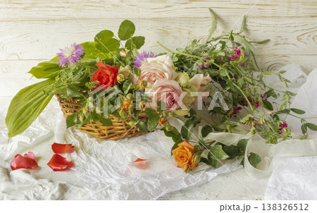 Fresh flower arrangement with roses and wildflowers in a wicker basket. Rustic flower arrangement with flowers from the garden. 138326512