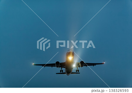 Airplane approaching for landing with landing lights illuminated against a twilight sky, showcasing the aircraft's silhouette and atmospheric lighting effects Airplane approaching for landing with landing lights illuminated against a twilight sky, showcasing the aircraft's silhouette and atmospheric lighting effects 138326593