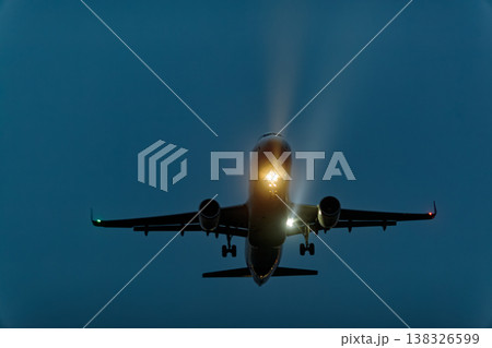 Airplane approaching for landing at dusk with landing lights illuminated, showcasing the aircraft's silhouette against a darkening sky 138326599