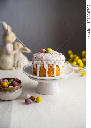 Easter festive cake with icing, sprinkles and eggs candy. White egg and spring, yellow flower twigs. Easter festive cake with icing, sprinkles and eggs candy. White egg and spring, yellow flower twigs. 138326707