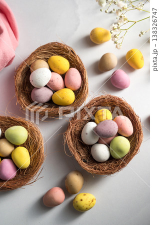 Easter holiday Spring background with mini eggs candy in nests over bright background Easter holiday Spring background with mini eggs candy in nests over bright background 138326747