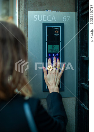 Woman with multiple rings pressing intercom button at building entrance, displaying the name 'SUECA' and number '67' on the panel Woman with multiple rings pressing intercom button at building entrance, displaying the name 'SUECA' and number '67' on the panel 138326757