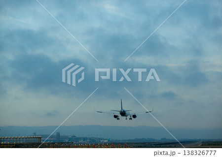 Airplane landing at airport runway during twilight with clouds in the sky and airport buildings visible in the background Airplane landing at airport runway during twilight with clouds in the sky and airport buildings visible in the background 138326777