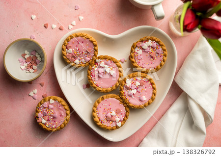 Valentine's day dessert. Pink mini tarts with heart shaped sprinkles in heart plate. Top view Valentine's day dessert. Pink mini tarts with heart shaped sprinkles in heart plate. Top view 138326792