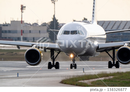 Commercial airplane taxiing on runway at airport with terminal buildings and control tower visible in the background during daylight hours Commercial airplane taxiing on runway at airport with terminal buildings and control tower visible in the background during daylight hours 138326877