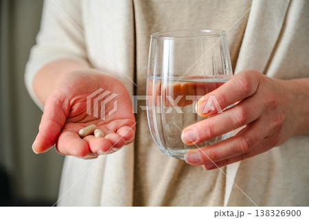 Woman holding two capsules pills in one hand and a glass with water, in other. Prescription medication, treatment sickness, seasonal cold flu concept Woman holding two capsules pills in one hand and a glass with water, in other. Prescription medication, treatment sickness, seasonal cold flu concept 138326900