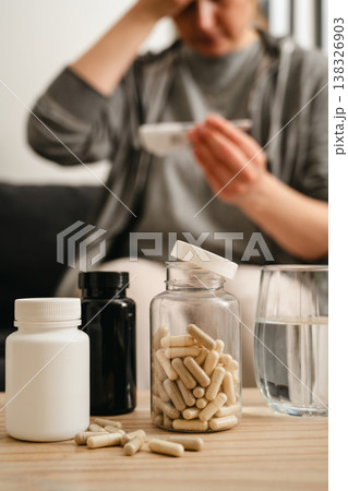 Medical treatment, jar with pills on the table and a woman on background measuring fever. Medical treatment, jar with pills on the table and a woman on background measuring fever. 138326903