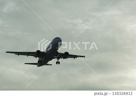 Commercial airplane flying through cloudy sky during sunset, with landing gear deployed and wings extended, capturing the essence of air travel and aviation 138326912
