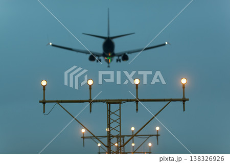 Airplane approaching landing with illuminated runway lights visible in the foreground against a cloudy sky during twilight hours Airplane approaching landing with illuminated runway lights visible in the foreground against a cloudy sky during twilight hours 138326926