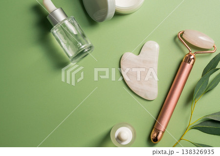 Rose quartz gua sha tool and face massage roller on green background, beauty abstract photo. Top view Rose quartz gua sha tool and face massage roller on green background, beauty abstract photo. Top view 138326935