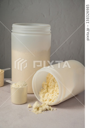 Protein powder in scoops with white plastic protein tubes, jars in background. Body building, muscle growth and food supplement concept Protein powder in scoops with white plastic protein tubes, jars in background. Body building, muscle growth and food supplement concept 138326985