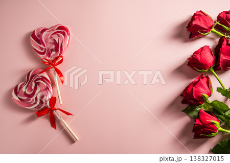 Valentine's Day background. Red roses and heart shaped lolly candy over pink background. Abstract flat lay. Celebrate, festive greeting card. Valentine's Day background. Red roses and heart shaped lolly candy over pink background. Abstract flat lay. Celebrate, festive greeting card. 138327015