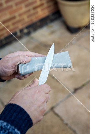 Man 's hand sharpening the kitchen knife with whetstone outdoor 138327050