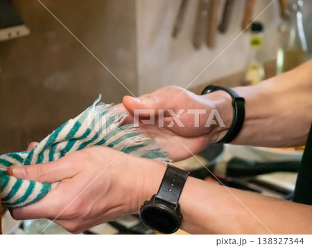 Man hands drying with striped cloth in rustic kitchen. Male person wiping palms with towel after preparing food. Domestic life chore, cooking prep and hygiene routine at home interior. Man hands drying with striped cloth in rustic kitchen. Male person wiping palms with towel after preparing food. Domestic life chore, cooking prep and hygiene routine at home interior. 138327344