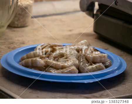 Raw shrimp in blue plate on kitchen counter. Fresh crustacean seafood prepared for cooking. Ingredient for healthy diet and culinary meal recipe concept. High protein food preparation. Raw shrimp in blue plate on kitchen counter. Fresh crustacean seafood prepared for cooking. Ingredient for healthy diet and culinary meal recipe concept. High protein food preparation. 138327348