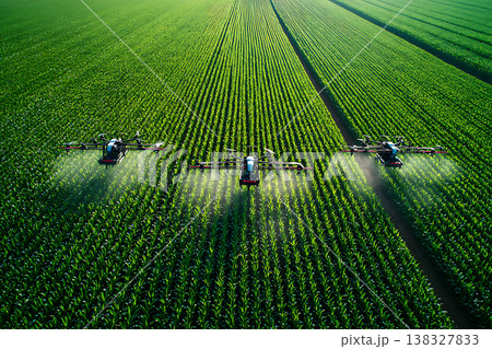 Three drones apply treatment to rows of green crops in a large farm field 138327833