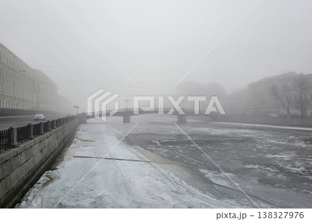 Fog blankets a quiet city street. Lone car glides through misty gloom Fog blankets a quiet city street. Lone car glides through misty gloom 138327976