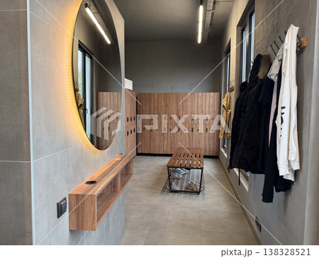 Modern locker room interior with wooden lockers bench mirror and hanging clothes in sports facility. Changing area usage, storage organization, fitness infrastructure and daily routine concept Modern locker room interior with wooden lockers bench mirror and hanging clothes in sports facility. Changing area usage, storage organization, fitness infrastructure and daily routine concept 138328521