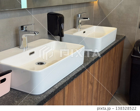 Double ceramic sinks with chrome faucets installed on stone countertop in shared restroom. Hygiene routine, simultaneous usage, public facility design and sanitation efficiency concept 138328522