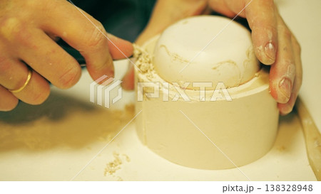 Close up of potter refining the edge of a plaster slip casting mold with a knife in a ceramics workshop Close up of potter refining the edge of a plaster slip casting mold with a knife in a ceramics workshop 138328948