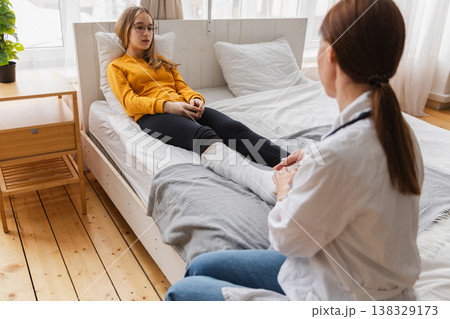 Girl with broken leg and doctor in clinic. Traumatologist orthopedist examines child leg in medical office. Doctor examining girl with medical plaster leg cast after broken ankle injury Rehabilitation 138329173