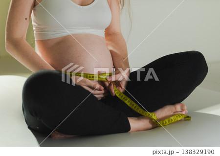 Pregnancy motherhood. Pregnant woman measuring big belly. Girl measuring her belly with tape to keep track of her fetus development. Woman enjoying pregnancy. Maternity tenderness parenthood new life 138329190