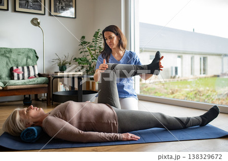 Physiotherapist exercising with older woman during rehabilitation session at home. Physiotherapist exercising with older woman during rehabilitation session at home. 138329672