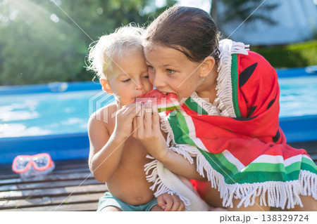 Sister and toddler brother eating watermelon after swimming in pool. 138329724